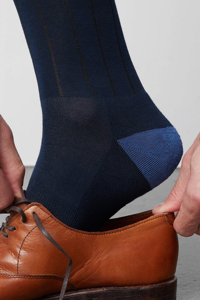 Side view of a man putting on a shoe and wearing Silver Extended Crew Dress Sock in True Navy
