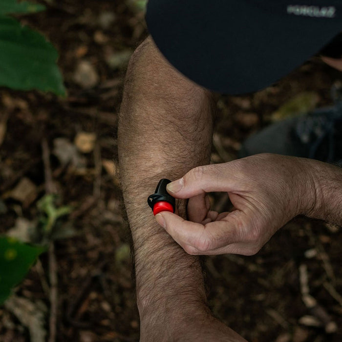 Lifestyle photograph of a man using a Lifesystems mini insect bite relief clicker on his arm in the jungle