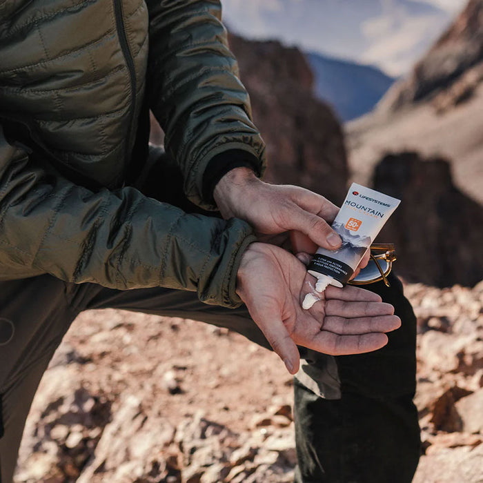 Lifestyle image of a man applying Lifesystems Mountain sun cream from a 50ml bottle to the palm of his hands whilst climbing mountains