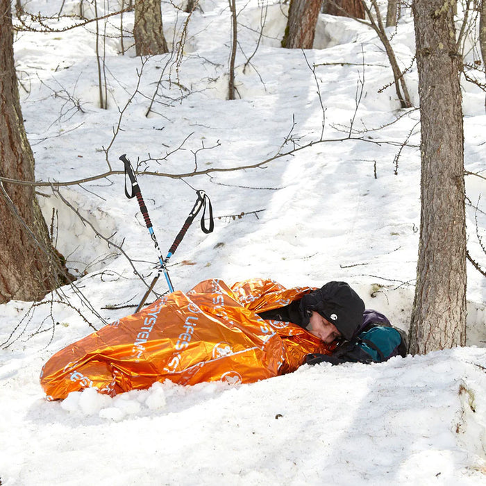 Lifestyle image of a man using a lifesystems thermal bag whilst sleeping in the snow amongst trees in winter