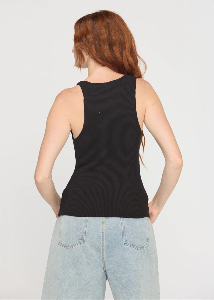 Woman turned around wearing a notch neck black tank top with denim shorts and a belt