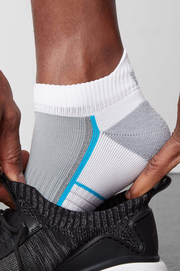Side view of a man putting on a shoe and wearing AIRKNITx Ankle Sock in Bright White / Weldon Blue