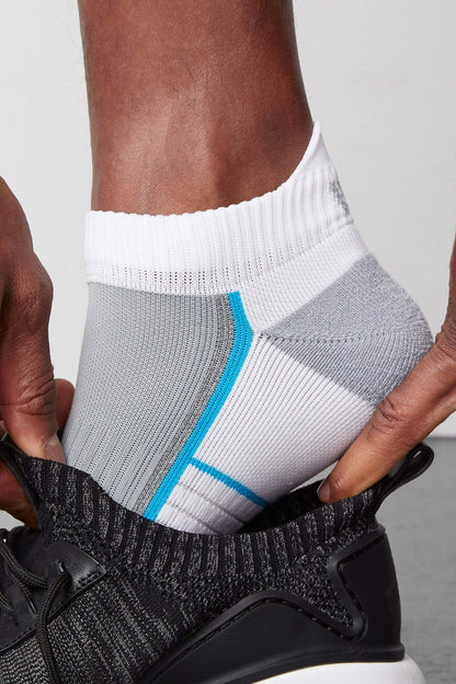 Side view of a man putting on a shoe and wearing AIRKNITx Ankle Sock in Bright White / Weldon Blue