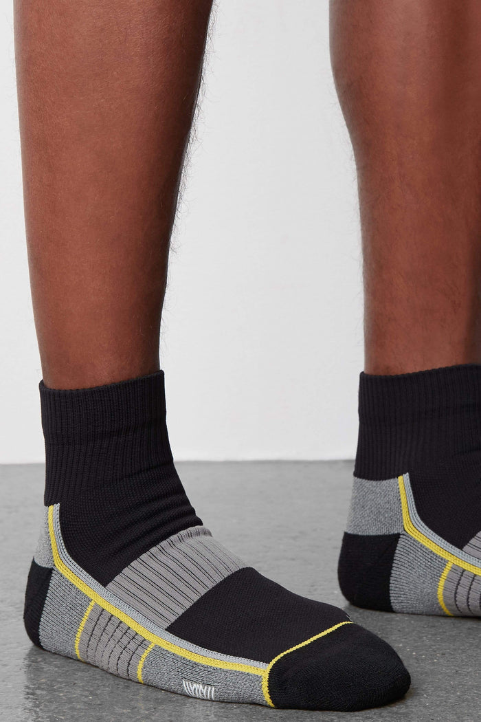 Side view of a man wearing AIRKNITx High Ankle Sock in True Black /Taxi