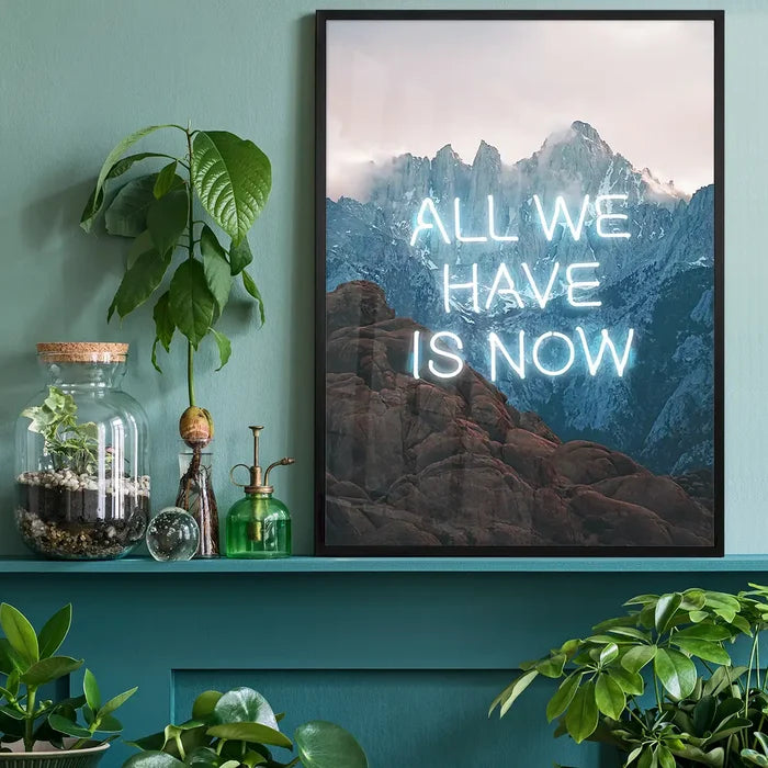 Framed All We Have Is Now neon mountain art print on a teal wall with indoor plants and a glass terrarium.