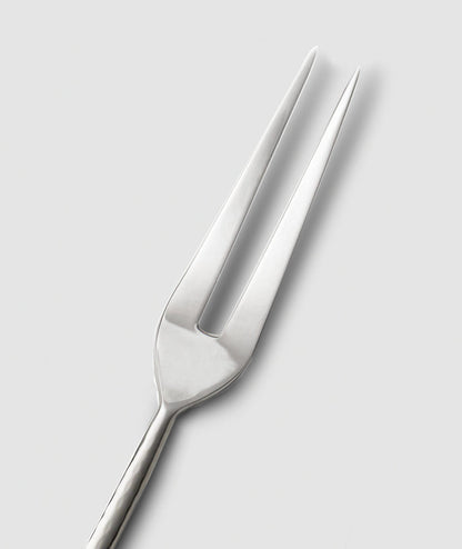 The Mary Jurek Alta Meat Serving Fork, with its two long, pointed tines, is set diagonally on a plain light gray background—an elegant stainless steel addition to your serving utensils.