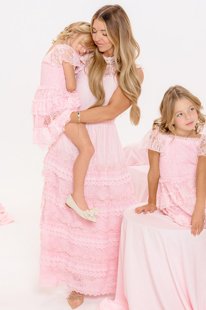 A woman and two young girls with long blonde hair wear matching Ivy City Co Annie Dresses in Light Pink, surrounded by soft pink fabrics.