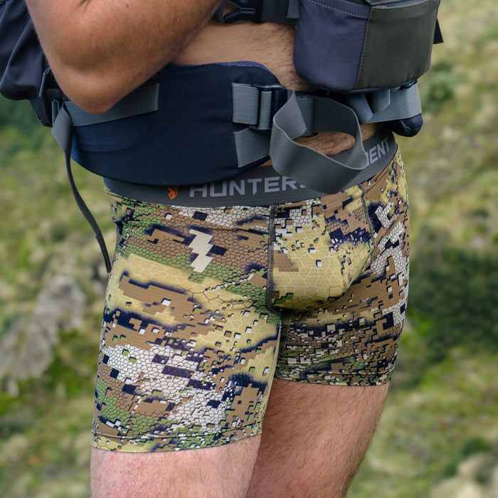 Person wearing camouflage shorts with a hunting vest in a natural setting