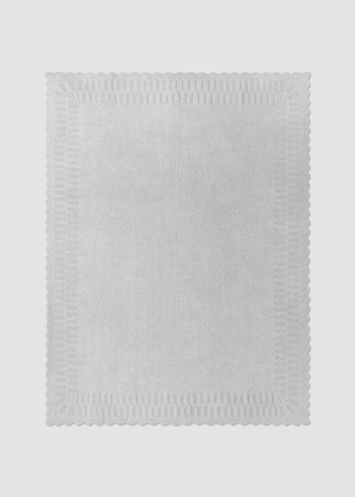 Grey blanket with scallop edges laying on a grey background