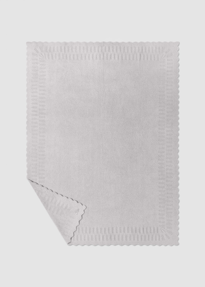 Grey blanket with scallop edges laying on a grey background with a corner folded