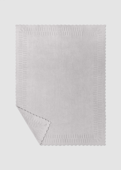 Grey blanket with scallop edges laying on a grey background with a corner folded