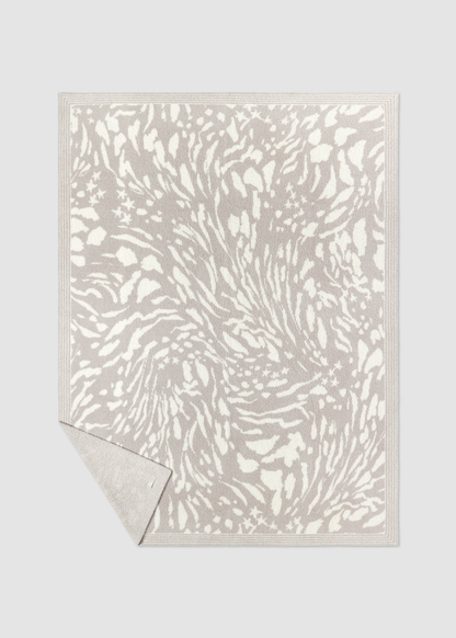 Grey and cream animal print blanket laying on a grey background with a corner folded