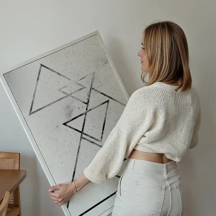 Woman holding a framed abstract black triangle print on textured white paper.
