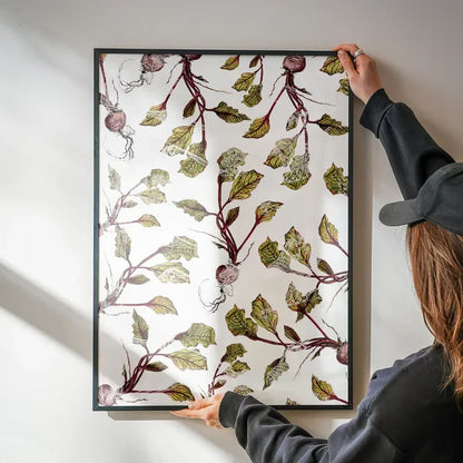 Person holding a framed Botanical Beetroot print with green leaves and purple roots on white archival paper.