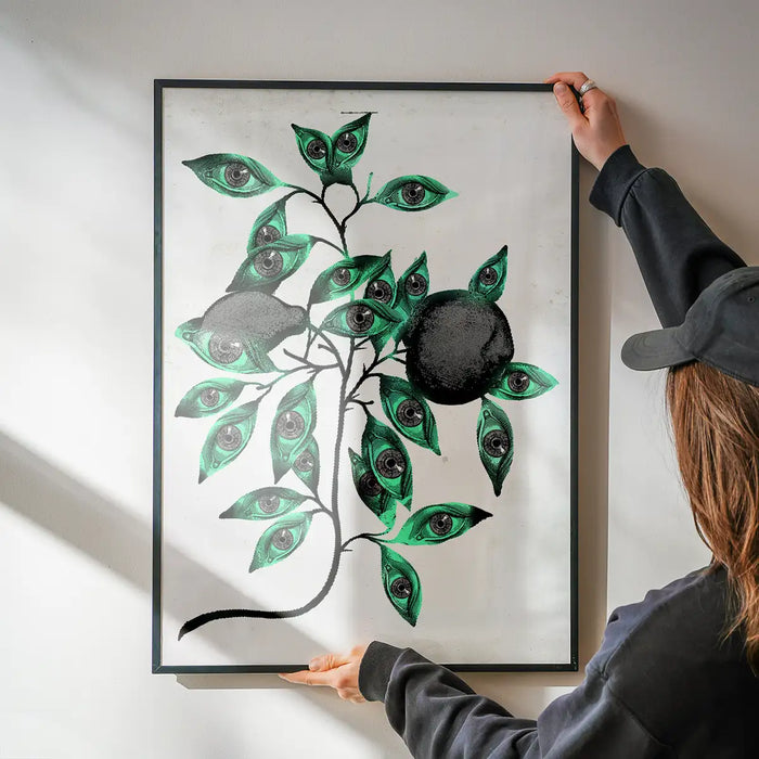 Striking framed Botanical Eyes print with green leaves and dark eyes, held against a white wall.