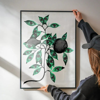 Striking framed Botanical Eyes print with green leaves and dark eyes, held against a white wall.