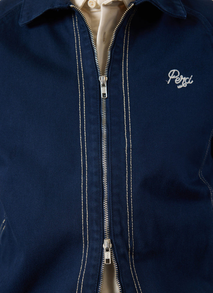 A close-up of the navy Calabria Harrington Jacket by Percival, showing the zip, contrast stitching, and 'Perci' logo.