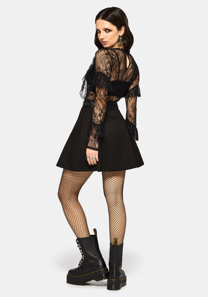 Woman wearing a black lace top, black skirt, and black boots on a white studio background