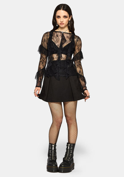 Woman wearing a black lace top, black mini skirt with black fishnet tights and black platform boots on a white studio background