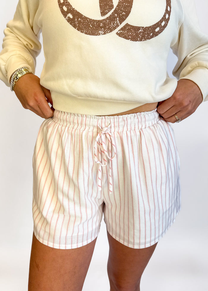 Person wearing a beige sweatshirt with a logo and striped shorts on a white background