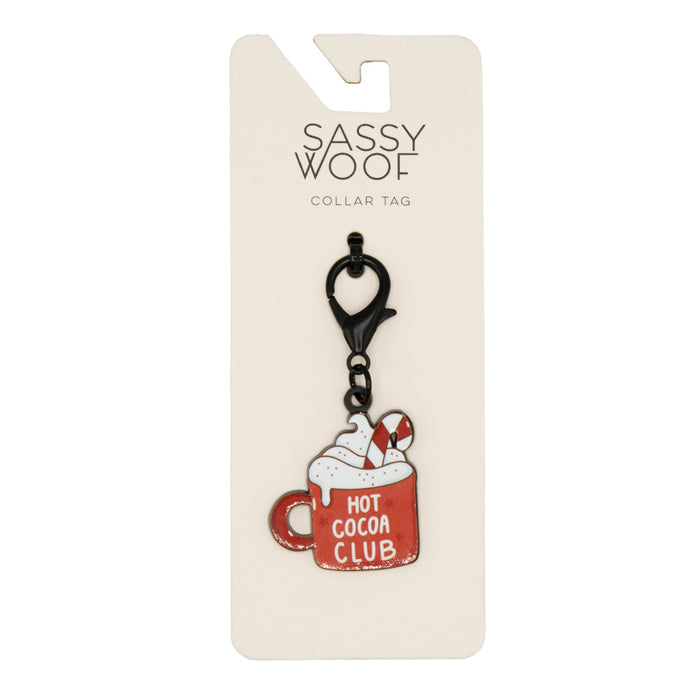 The Sassy Woof Collar Tag - Hot Cocoa Club features a red mug with whipped cream, sprinkles, and a candy cane—ideal for holiday pet accessories. Comes attached to a cream-colored backing card.