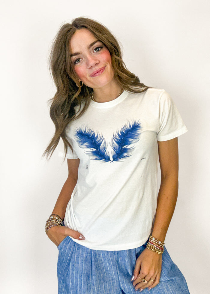 Woman wearing a white t-shirt with blue feather design on a plain background