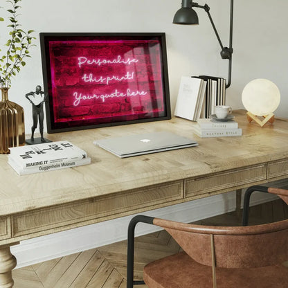 Framed neon-style print featuring glowing pink cursive text on a red brick background, displayed on a wooden desk.