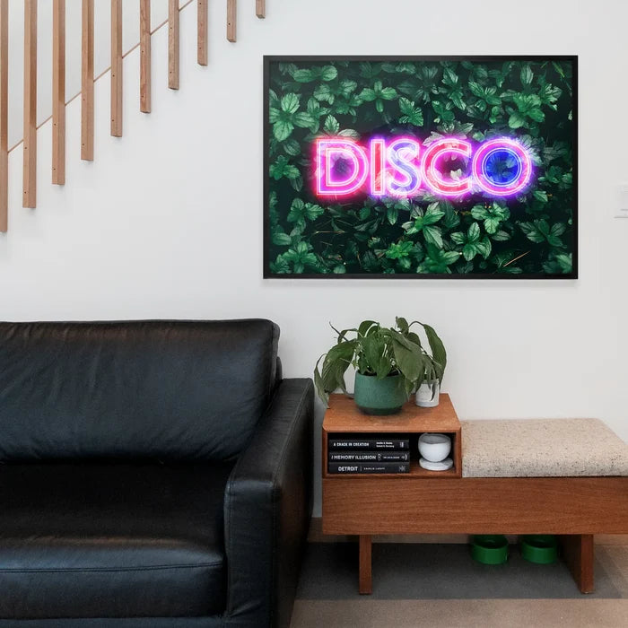 Framed wall art featuring a glowing pink and blue neon DISCO sign set against a lush green botanical leaf background.