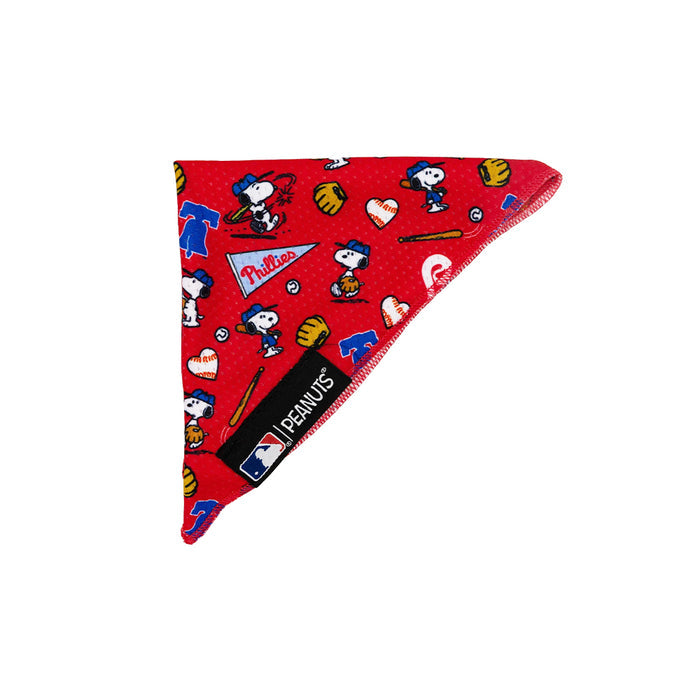 The Sassy Woof Dog Bandana - MLB™ x Peanuts™ Philadelphia Phillies™ is a red pet bandana featuring Snoopy in baseball gear with gloves, bats, hearts, Phillies logos, and official MLB Peanuts tags on the edge.