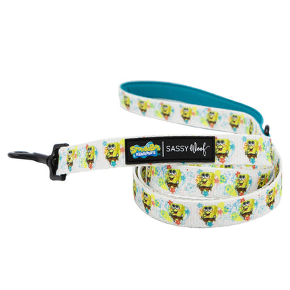 A white dog leash from the Dog Collar Three Piece Bundle - SpongeBob SquarePants™ Bikini Bottom by Sassy Woof, featuring colorful SpongeBob SquarePants graphics, a black clip, and a label that reads "SpongeBob SquarePants" and "Sassy Woof." Part of the official line of SpongeBob pet accessories, this playful leash is designed with a blue inner lining for added comfort and style.
