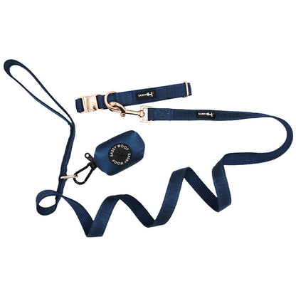 A Sassy Woof Dog Collar Three Piece Bundle in the Twilight Collection, featuring a navy blue leash with a loop handle and gold clasp, a matching collar, and a waste bag holder with roll of bags.