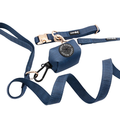 A blue Dog Collar Three Piece Bundle - Twilight from Sassy Woof, featuring a matching dog collar and leash, plus an attached waste bag holder with a circular “Sassy Woof” logo on the bag holder.