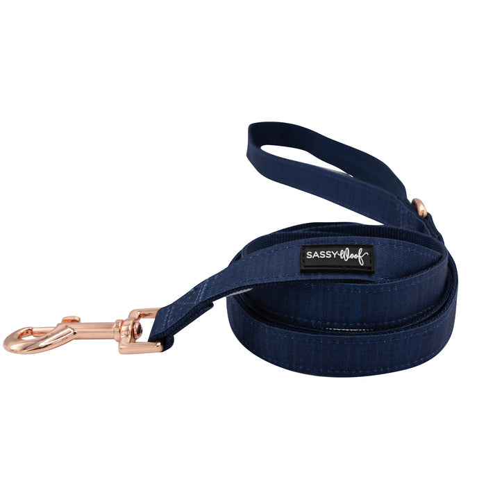 A navy blue dog leash from Sassy Woof’s Dog Collar Three Piece Bundle - Twilight, featuring a rose gold metal clasp and a black “SASSY WOOF” label, is coiled neatly on a white background. Pair it with the matching collar from the bundle for a perfectly coordinated look.