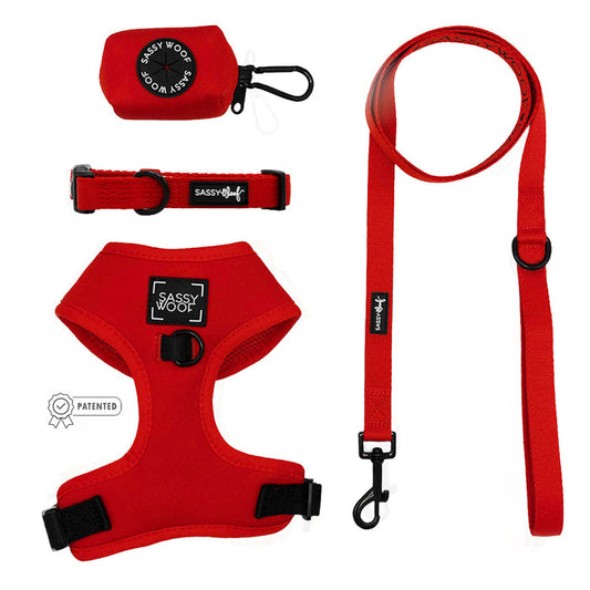 The Sassy Woof Dog Four Piece Bundle in Neon Red includes an adjustable harness, collar, leash, and waste bag holder—essentials for pups of all sizes—displayed on a white background.
