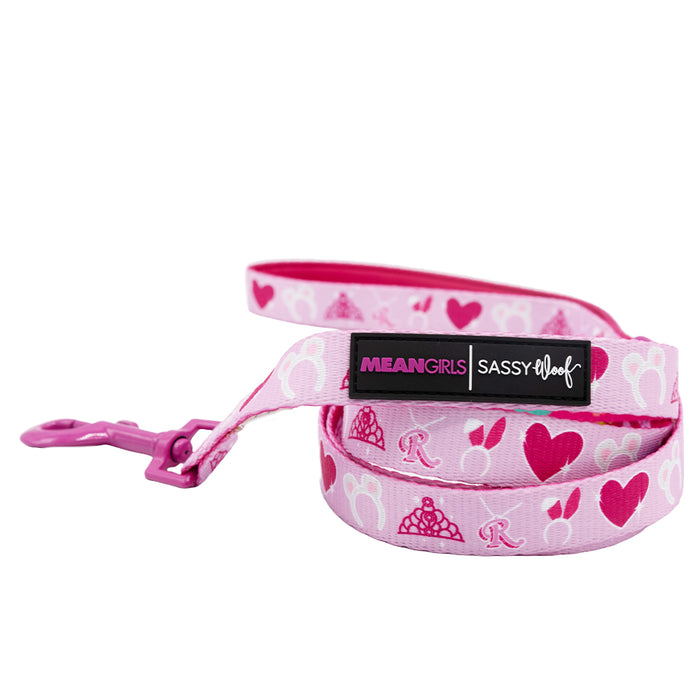 The Dog Leash - Mean Girls™ by Sassy Woof features a pink design with hearts, crowns, the letter R, a pink clip, and two labels—MEAN GIRLS and SASSY WOOF—perfect for matching your pup’s accessories.