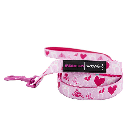 The Dog Leash - Mean Girls™ by Sassy Woof features a pink design with hearts, crowns, the letter R, a pink clip, and two labels—MEAN GIRLS and SASSY WOOF—perfect for matching your pup’s accessories.