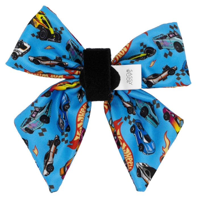 The Sassy Woof Dog Sailor Bow – Hot Wheels™ features blue fabric with colorful Hot Wheels cars, flames, and checkered flags, plus a black center band and white tag—ideal for fans of Hot Wheels dog accessories.