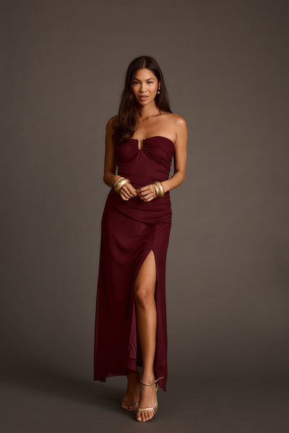 Burgundy strapless mesh maxi dress with a keyhole cutout and gold bangle bracelets.