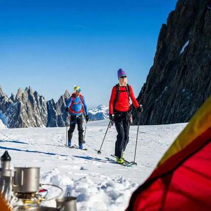 Lifestyle image of a woman and a man alpine skiing at altitude whilst wearing Sub Zero thermal mid layer long sleeve tops and bottoms