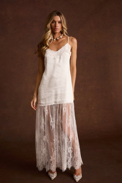 White satin slip dress with a lace trim neckline and sheer lace hem, styled with a pearl necklace.