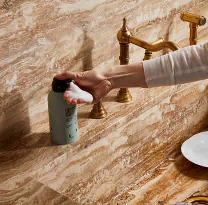 Guests on Earth Foaming Hand Soap dispensed at a marble sink, rich foam in hand beside brass tap