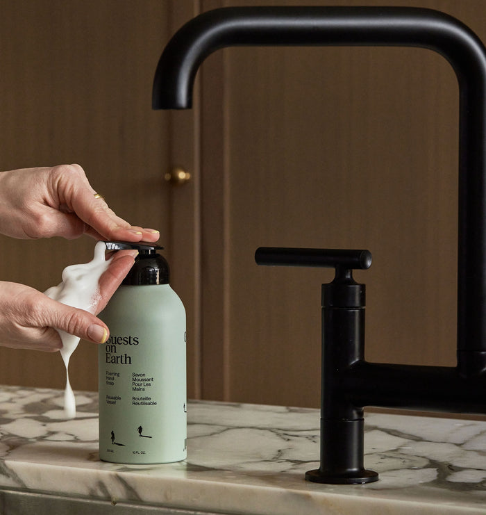 Guests on Earth Foaming Hand Soap dispensed in creamy foam beside matte black faucet on marble countertop