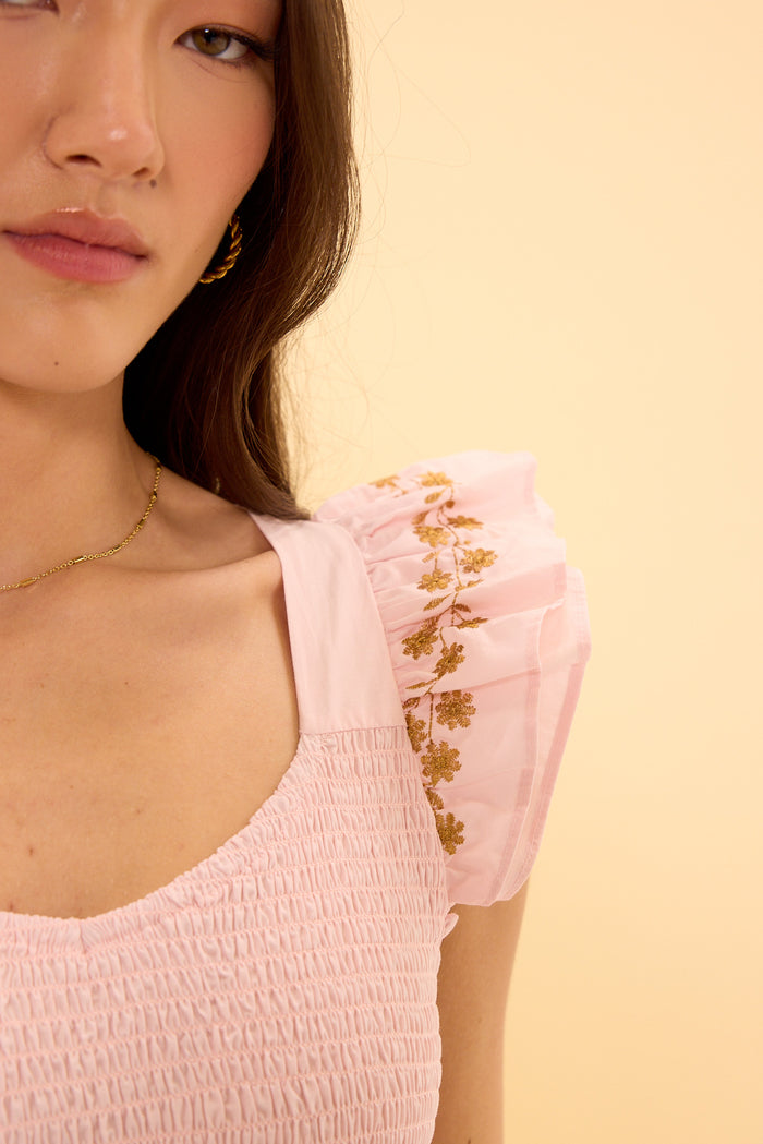 Close-up of a person wearing a pink top with floral embroidery on a beige background