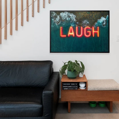 Framed wall art featuring a glowing red LAUGH neon sign set against a vibrant aerial ocean wave print.