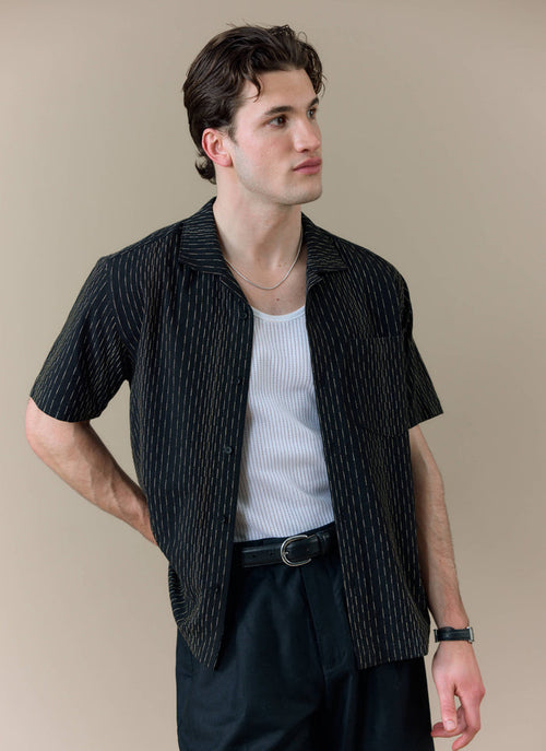 Model wearing the black Leland Cuban shirt by Percival, showing the subtle vertical stripe detail and Cuban collar.