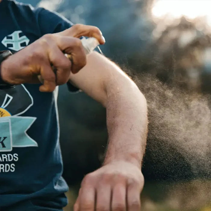 Man spraying his exposed arm with insect repellent whilst outdoors to protect against biting insects