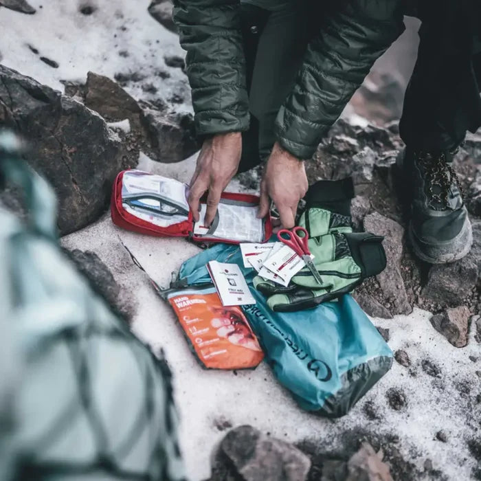 Person organising first aid supplies on a snowy ground using a Lifesystems Trek First Aid Kit