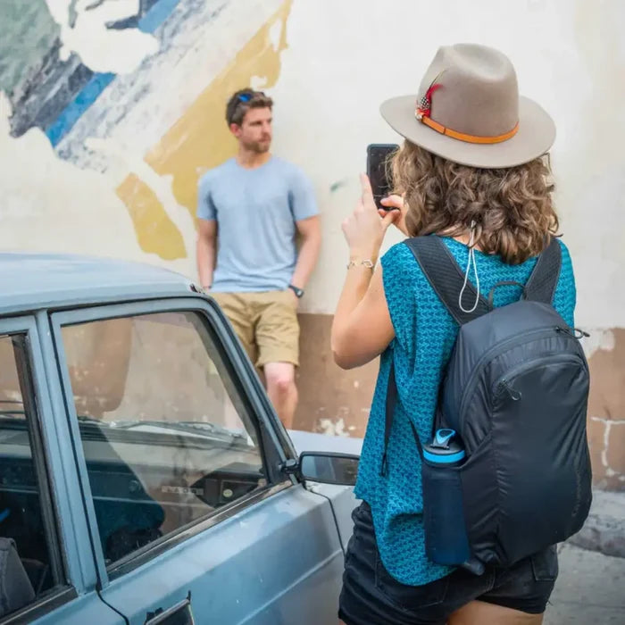 Person with a Lifeventure Packable Backpack in 16 Litres capacity in black taking a photo of another person standing next to a car.