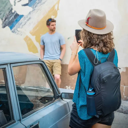 Person with a Lifeventure Packable Backpack in 16 Litres capacity in black taking a photo of another person standing next to a car.