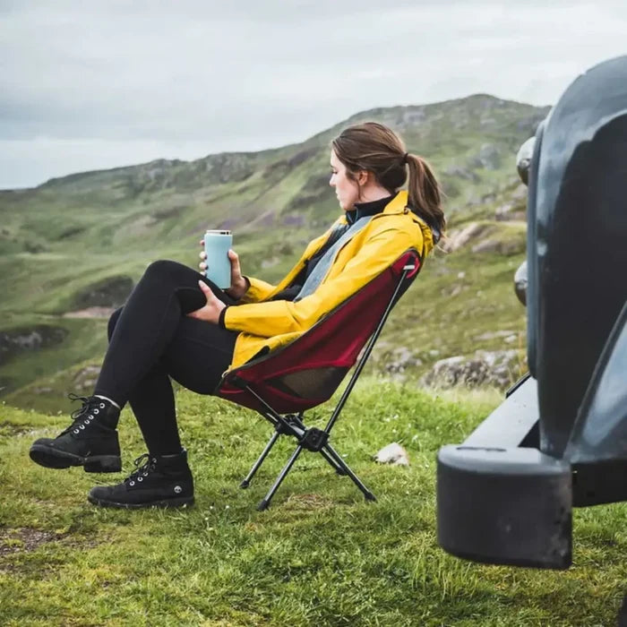 Person sitting in a red camping chair holding an ice blue Lifeventure thermal mug in a scenic outdoor setting